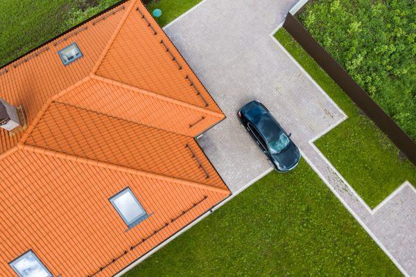 Aerial top view of house metal shingle roof with attic windows and black car on paved yard.