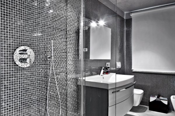 interior view of a modern bathroom in the foregorund the shower cubicle a little further on there is a sink cabinet with integrated washbasin the walls are covered with mosaic tiles